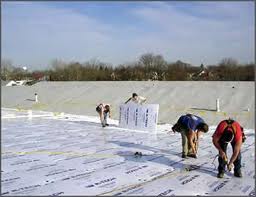 a group of laborers install commercial roofing one layer at at time on a flat tar roof